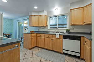 Kitchen featuring dark countertops, a peninsula, white dishwasher, light tile patterned floors, and recessed lighting