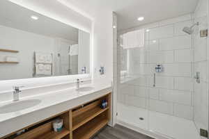 Full bathroom featuring double vanity, a stall shower, recessed lighting, and dark wood-style flooring