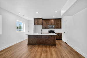 Kitchen featuring dark brown cabinetry, dark wood finished floors, stainless steel appliances, an island with sink, and recessed lighting