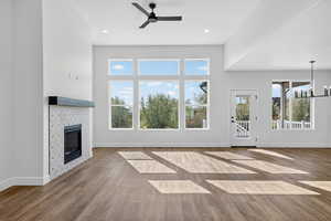 Unfurnished living room with wood finished floors, a chandelier, ceiling fan, a fireplace, and recessed lighting