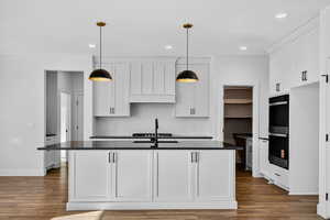 Kitchen featuring white cabinets, a kitchen island with sink, backsplash, stainless steel double oven, and dark wood finished floors