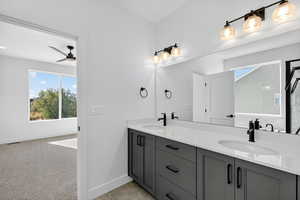 Full bath with double vanity, plenty of natural light, light carpet, and a ceiling fan