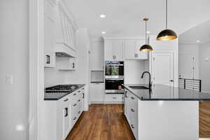 Kitchen with dark wood-type flooring, stainless steel appliances, recessed lighting, backsplash, and a center island with sink
