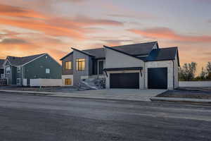 Modern home featuring driveway, a garage, stone siding, and roof with shingles