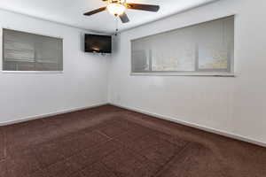 Empty room featuring dark carpet and a ceiling fan