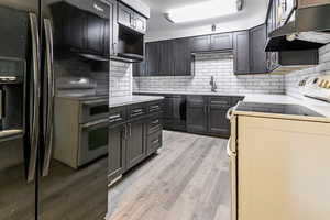Kitchen with black appliances, decorative backsplash, and under cabinet range hood