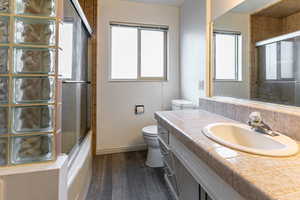 Full bathroom with vanity, dark wood-style flooring, and bath / shower combo with glass door