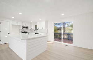 Kitchen with a kitchen island, white cabinetry, tasteful backsplash, stainless steel appliances, and light wood-style floors