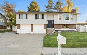 Bi-level home with brick siding, a chimney, concrete driveway, and an attached garage