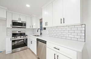 Kitchen featuring stainless steel appliances, white cabinetry, light wood-type flooring, light stone counters, and recessed lighting