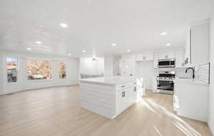 Kitchen with stainless steel appliances, white cabinetry, a center island, open floor plan, and tasteful backsplash