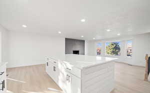 Kitchen with white cabinets, light wood finished floors, a center island, recessed lighting, and open floor plan