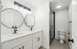 Full bath with light wood-style flooring, double vanity, a shower stall, and a textured ceiling