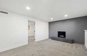 Unfurnished living room featuring a fireplace, light colored carpet, recessed lighting, and wooden walls