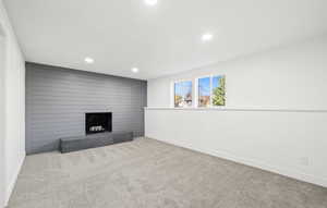 Unfurnished living room featuring carpet, recessed lighting, a fireplace, and wooden walls