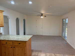 Kitchen with light stone countertops, light carpet, a ceiling fan, arched walkways, and open floor plan