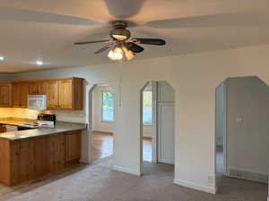 Kitchen with light carpet, light stone countertops, white appliances, a peninsula, and arched walkways