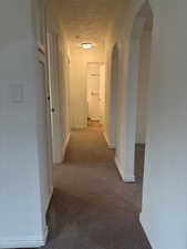 Hall featuring arched walkways and light carpet