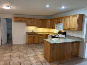 Kitchen featuring light stone countertops, white appliances, a peninsula, light tile patterned floors, and recessed lighting