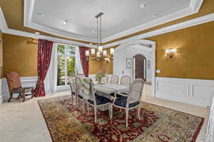 Dining area featuring wainscoting, a tray ceiling, arched walkways, a chandelier, and a decorative wall