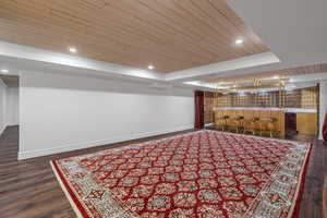 Finished basement featuring wooden ceiling, dark wood-style floors, recessed lighting, ornamental molding, and wet bar