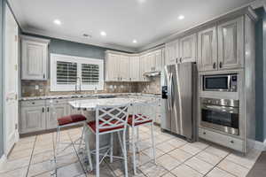 Kitchen with stainless steel appliances, light stone counters, a breakfast bar, recessed lighting, and crown molding
