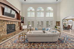 Living area featuring ceiling fan, plenty of natural light, ornamental molding, a stone fireplace, and a high ceiling