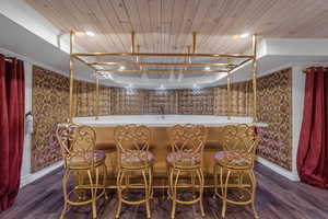 Indoor wet bar featuring dark wood finished floors, wooden ceiling, recessed lighting, brown cabinetry, and ornamental molding