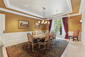 Dining area with wainscoting, a decorative wall, a chandelier, a raised ceiling, and crown molding