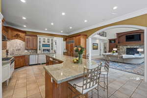 Kitchen with arched walkways, brown cabinets, a breakfast bar area, glass insert cabinets, and decorative backsplash
