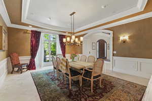 Dining space with wainscoting, a decorative wall, a raised ceiling, arched walkways, and a chandelier
