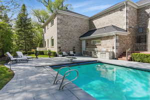 Rear view of property with a patio, exterior kitchen, an outdoor pool, and brick siding