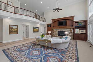 Living room with a towering ceiling, a stone fireplace, ornamental molding, recessed lighting, and a ceiling fan