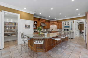 Kitchen featuring brown cabinets, recessed lighting, light tile patterned flooring, light stone counters, and crown molding