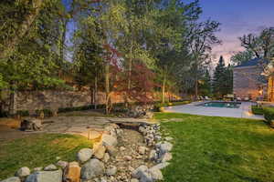 Yard at dusk with a patio, a lawn, and view of wooded area