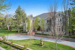 View of front of property featuring a front lawn, stone siding, a balcony, and a chimney