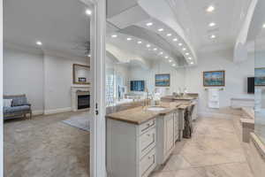 Kitchen with open floor plan, a fireplace, ornamental molding, light stone counters, and recessed lighting