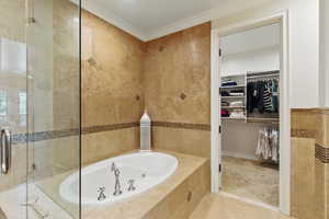 Bathroom featuring tile walls, a whirlpool tub, a walk in closet, crown molding, and a shower stall