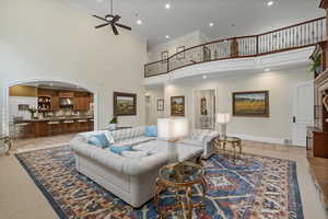 Living area with a towering ceiling, arched walkways, recessed lighting, light tile patterned flooring, and light colored carpet
