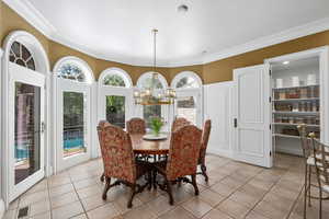 Dining area with light tile patterned floors, a chandelier, and ornamental molding