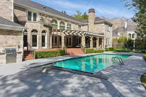 Rear view of house with a patio area, an outdoor pool, exterior kitchen, a balcony, and brick siding