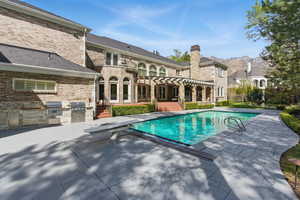 Outdoor pool with exterior kitchen, a patio area, a diving board, and a pergola
