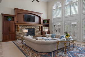 Living room featuring a stone fireplace, ornamental molding, a towering ceiling, carpet, and ceiling fan