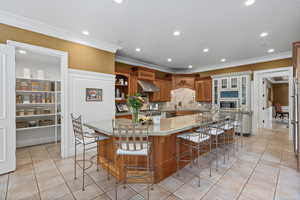 Kitchen with brown cabinets, recessed lighting, light tile patterned floors, a large island with sink, and light stone counters