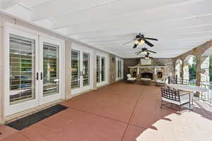 View of patio featuring a stone fireplace, ceiling fan, outdoor dining area, and french doors