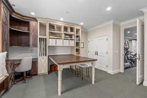 Office space with dark colored carpet, recessed lighting, ornamental molding, and built in desk