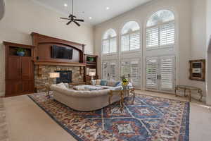 Carpeted living area featuring a high ceiling, a stone fireplace, ceiling fan, ornamental molding, and recessed lighting