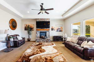 Living area with light colored carpet, a fireplace, a tray ceiling, and ceiling fan