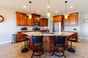 Kitchen with brown cabinets, tasteful backsplash, an island with sink, arched walkways, and recessed lighting