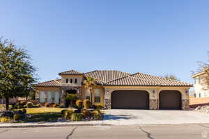 Mediterranean / spanish-style home with stone siding, stucco siding, an attached 3 car garage, and driveway.